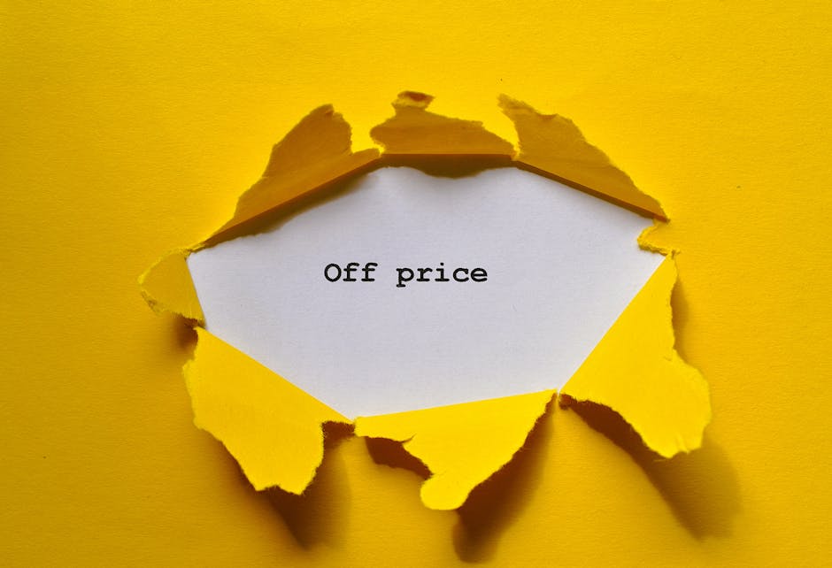 A close-up image features a jagged tear in a bright yellow paper surface, revealing a white piece of paper beneath with the partially visible text 'Off price' typed in black. The torn edges of the yellow paper curl outward, creating a three-dimensional opening that suggests a sudden break or removal. The background and surrounding area are uniformly yellow, highlighting the tear and the message inside. The scene appears to be set on a flat, smooth surface, with natural or diffuse lighting casting soft shadows around the torn edges. This visual metaphor can be associated with clearance sales, discounted or off-price items, and is relevant to household moving services such as those offered by Man With a Van Northwood, particularly in the context of packing and logistics for home relocation or furniture transport.